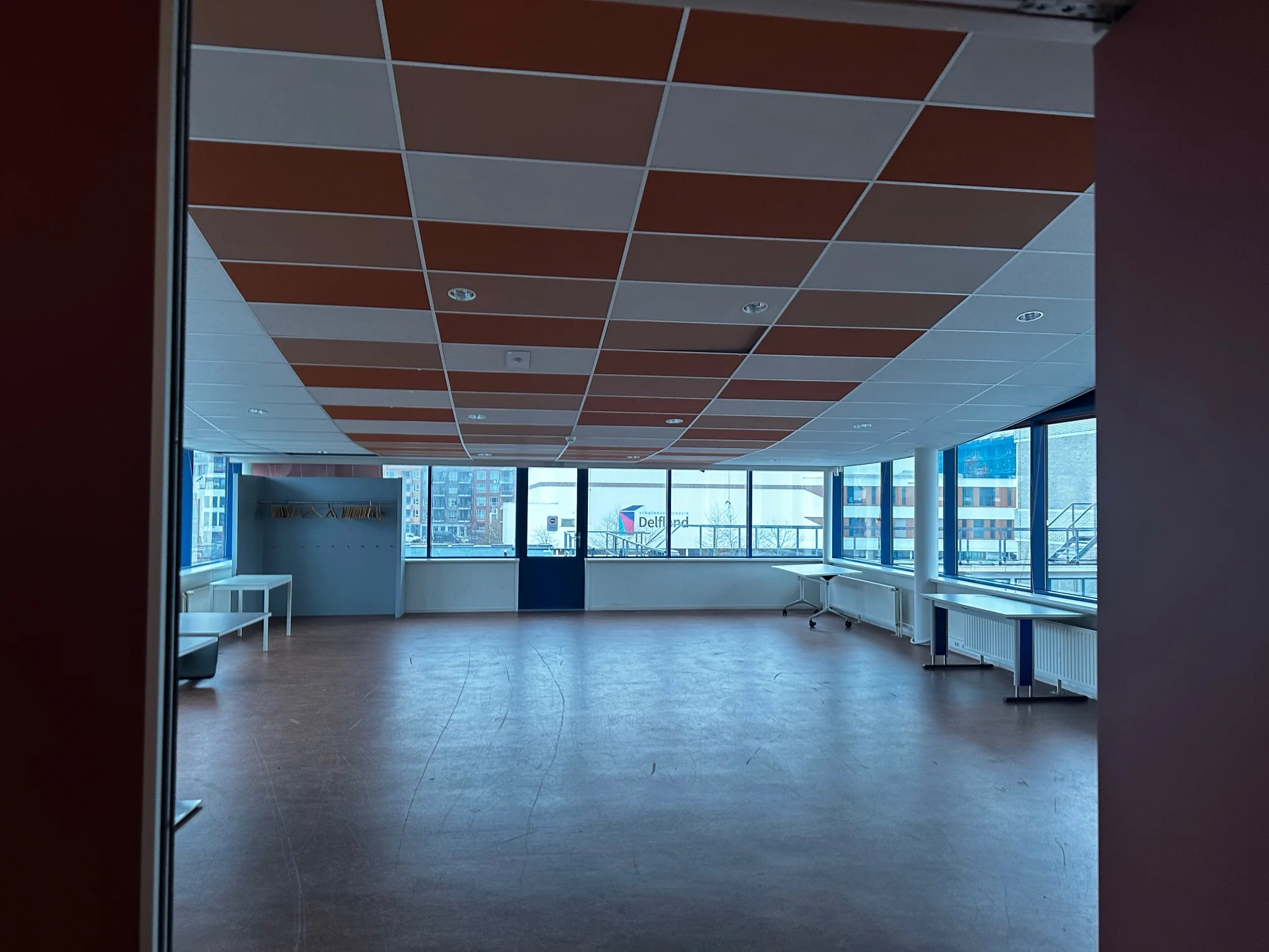 Leeg klaslokaal aan de Van Bleyswijckstraat met grote ramen en oranje-wit plafond.